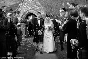 The bride and groom are covered in confetti by guests as they leave the church on their wedding day. The wedding was held at Apuldram Church, St Mary the Virgin Church, Apuldram, Chichester, West Sussex.